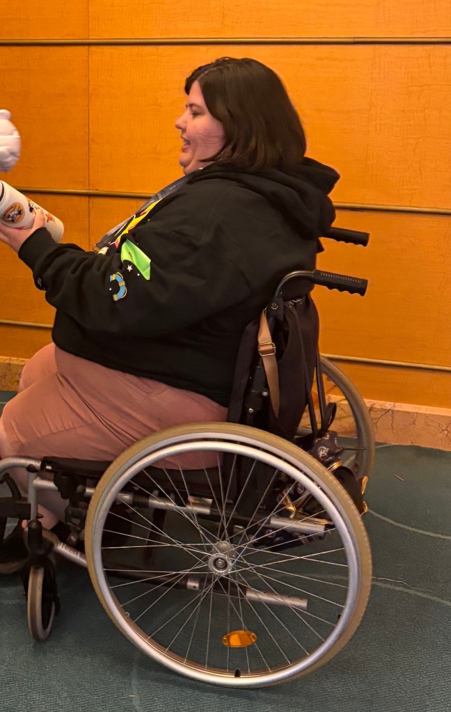 Krista in her Wheelchair, facing to the left of the image, interacting with someone out of frame.